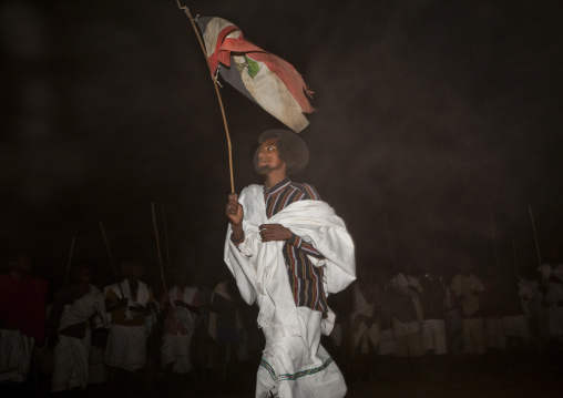Night Shot Of A Young Karrayyu Tribe Man In Traditional Clothes Dancing With Oromo Flag During Gadaaa Ceremony, Metahara, Ethiopia
