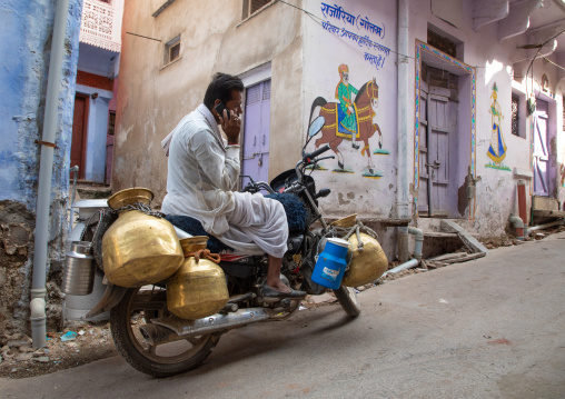 Indian man calling on his phone to deliver fresh milk with his motorbike, Rajasthan, Bundi, India