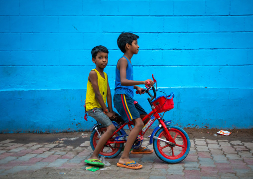 Indian boys riding a bicycle in front of a blue wall, Rajasthan, Jodhpur, India