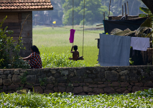 Young Child Sitting On A Swing Near The Backwaters Of Kerala, Alleppey, India