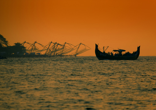 Boat Sailing Close To Chinese Fishing Nets In Silhouette At Sunset, Kochi, India