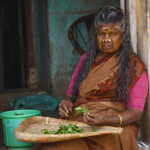 Old Woman With Double Nose Piercing Sitting On The Doorstep Of A House Sorting Out Green Leafes, Trichy, India