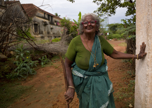 Old Woman With Glasses Holding Herself Against A Wall In A Garden In Kanadukathan Chettinad, India