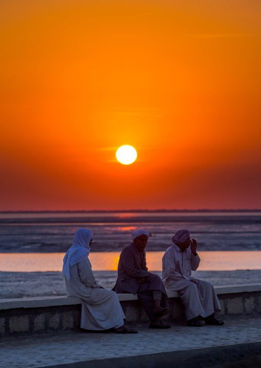 men dressed in traditional dress, sitting on a bench in front of the sunset, Qeshm Island, Laft, Iran