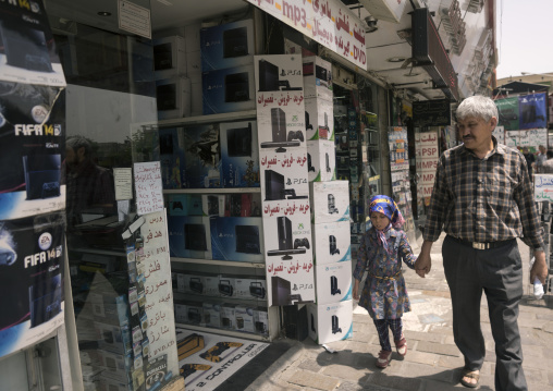 Father and daughter passing in front of an electronics shops, Shemiranat county, Tehran, Iran