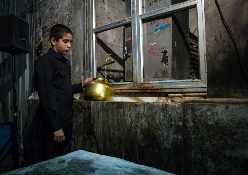 Boy collecting water in a pot to make tea in the bazaar for nazri during Muharram, Isfahan Province, Isfahan, Iran