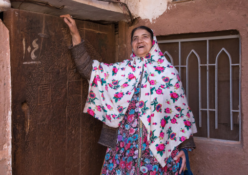 Portrait of an iranian woman wearing traditional floreal chador in front of an old wooden door, Natanz County, Abyaneh, Iran