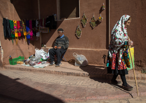 Iranian woman wearing traditional floreal chador and man selling souvenirs for tourists, Natanz County, Abyaneh, Iran