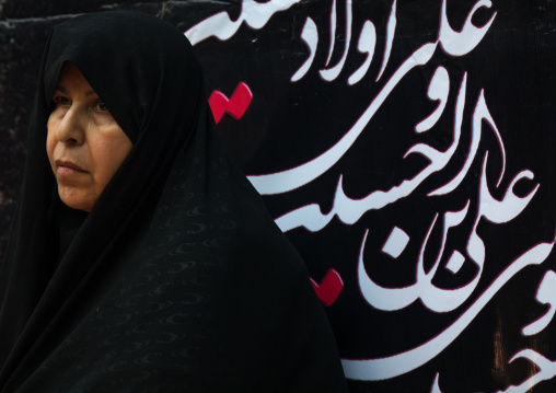 Iranian shiite woman in front of a billboard with calligraphy during Muharram to commemorate the martyrdom anniversary of Hussein, Lorestan Province, Khorramabad, Iran