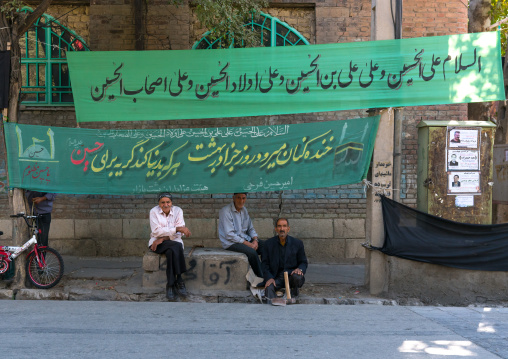 Men sit in the street under Muharram banners, Lorestan Province, Khorramabad, Iran