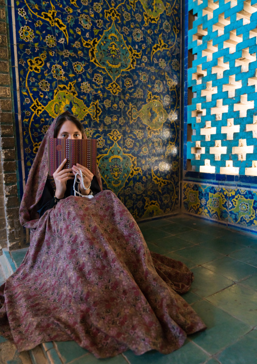 A young adult woman reads a book inside masjed-e Sheikh Lotfallah, Isfahan Province, Isfahan, Iran