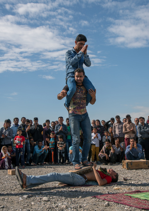 passers-by standing on the belly of a man lying on nail bed during a show on a market, Hormozgan, Minab, Iran