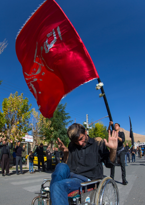 Man In Wheelchair In Front Of A Red Flag Celebrating Ashura, The Day Of The Death Of Imam Hussein, Kurdistan Province, Bijar, Iran