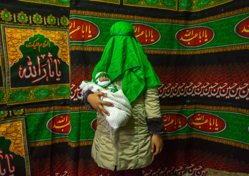 Iranian Woman With Green Veil Covering Her Face Holding A Baby Doll During Chehel Menbari Festival On Tasua To Commemorate Imam Hussein, Lorestan Province, Khorramabad, Iran