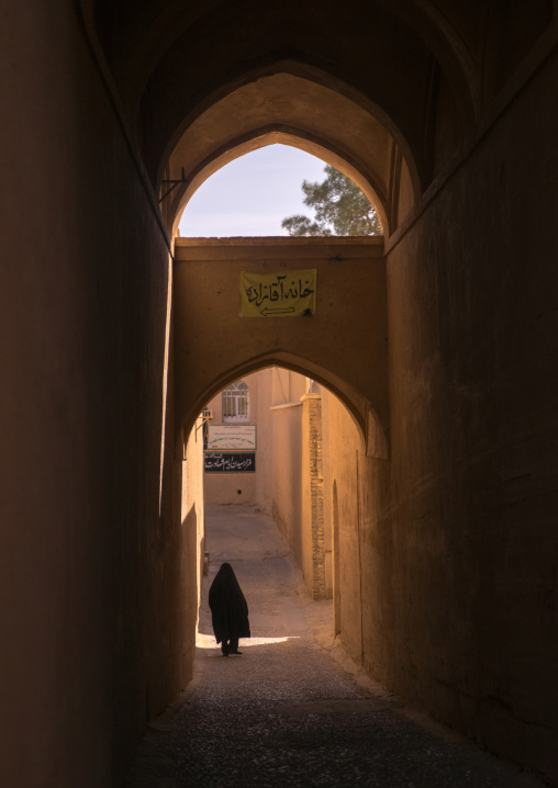 Elderly Muslim Woman Walking Under An Arch In A Narrow Street, Fars Province, Abarkooh, Iran