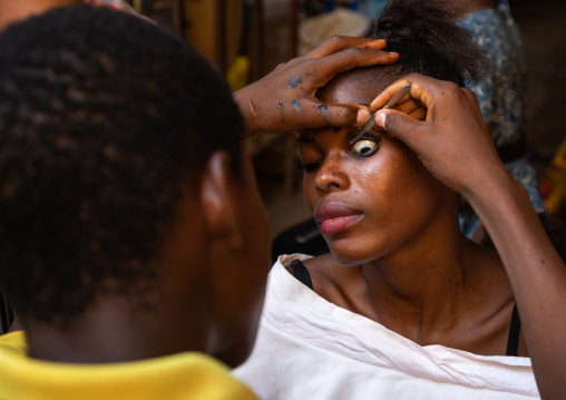 African man applying false eyelashes to a woman, Poro region, Korhogo, Ivory Coast