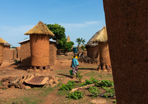Senufo woman carrying water passing in front granaries, Savanes district, Niofoin, Ivory Coast