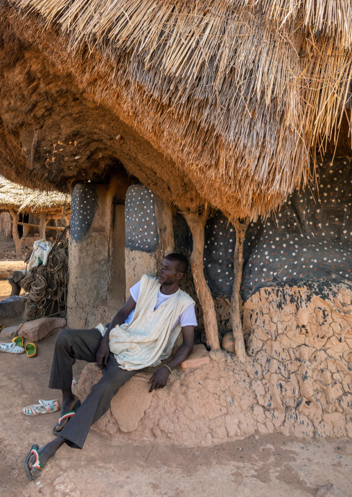 Senufo man sit in front of a fetish house whose roof gets a new layer every year, Savanes district, Niofoin, Ivory Coast