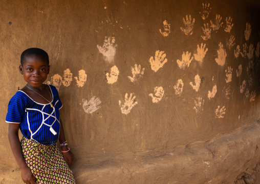 African girl standing in front of handprints on the wall of a hut, Bafing, Gboni, Ivory Coast