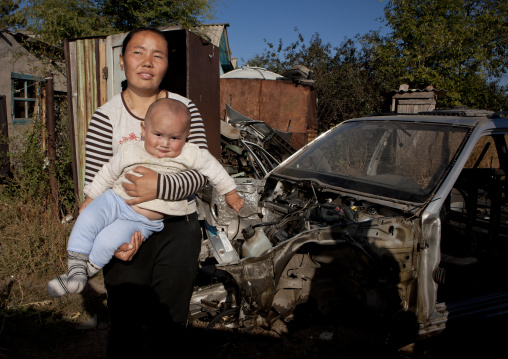 Woman With Her Baby In Front Of A Car Wreck In Her Garden, Astana, Kazakhstan
