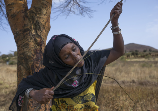 Borana woman cutting wood with her teeth to build a house, Marsabit district, Marsabit, Kenya