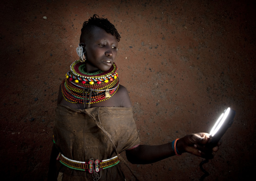 Turkana tribe woman with huge necklaces and earrings looking at a torch, Turkana lake, Loiyangalani, Kenya