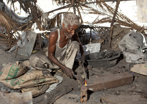 Blacksmith sweating while he forges nails, Lamu County, Lamu, Kenya