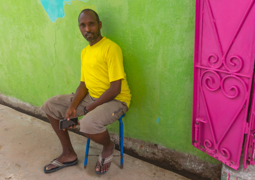 Kenyan man sit in the street in front of a colorful shop, Lamu county, Lamu town, Kenya