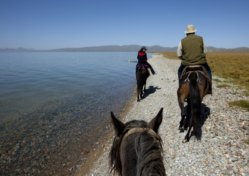 Woman And Western Man Riding Horses Along The Bank Of Song Kol Lake, Jaman Echki Jailoo, Kyrgyzstan