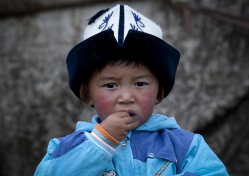 Boy With Traditional  Hat Putting His Fingers In His Mouth, Saralasaz Jailoo, Song Kol Lake Area, Kyrgyzstan