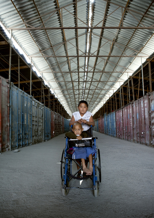 Boy Taking Care Of His Disabled Friend On A Wheelchair In Dordoi Market, Bishkek, Kyrgyzstan