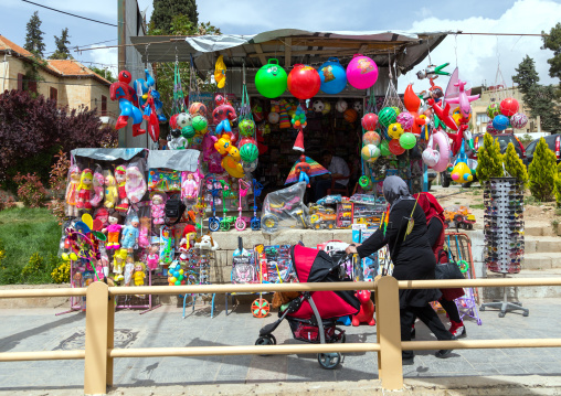 Lebanese woman with a baby-buggypassing in front of a toy shop with her child, Beqaa Governorate, Baalbek, Lebanon