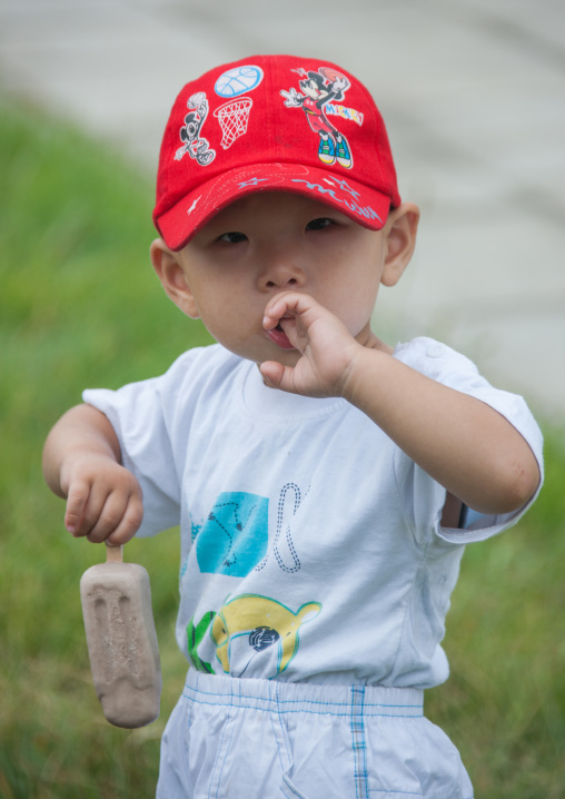 Portrait of a North Korean toddler with a Mickey mouse cap eating an ice cream, Pyongan Province, Pyongyang, North Korea