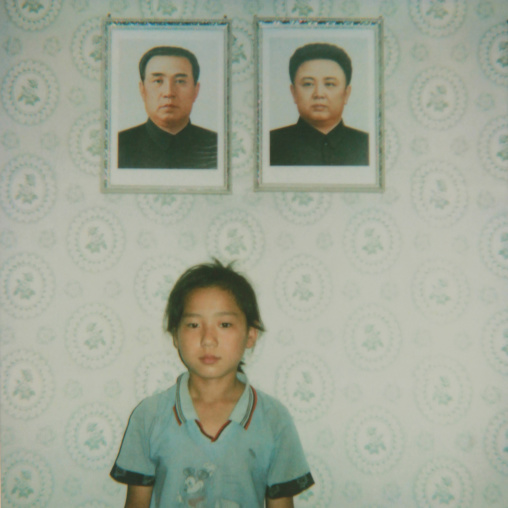 North Korean girl posing below the portraits of the Dear Leaders inside her home, South Pyongan Province, Chonsam Cooperative Farm, North Korea
