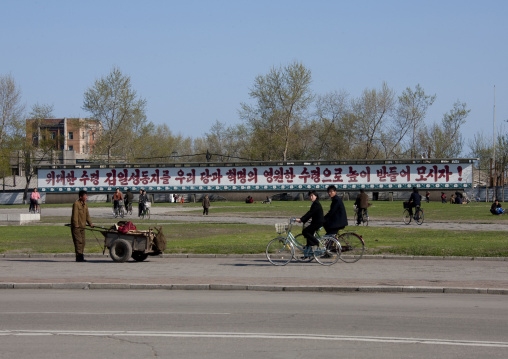 North Korean cyclists in a street in front of a propaganda billboard, North Hamgyong Province, Chongjin, North Korea