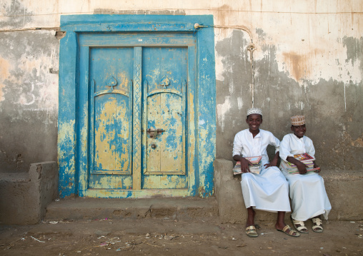 Two Kids In White Dishdasha Sitting Next To A Blue Wooden Door, Mirbat, Oman