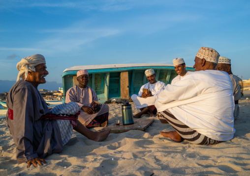 Omani men resting and drinking tea on the beach at sunset, Dhofar Governorate, Mirbat, Oman