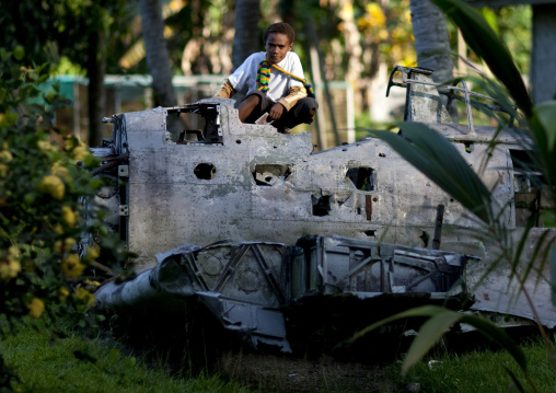 Boy sit on a plane wrecks in the war museum garden, East New Britain Province, Rabaul, Papua New Guinea