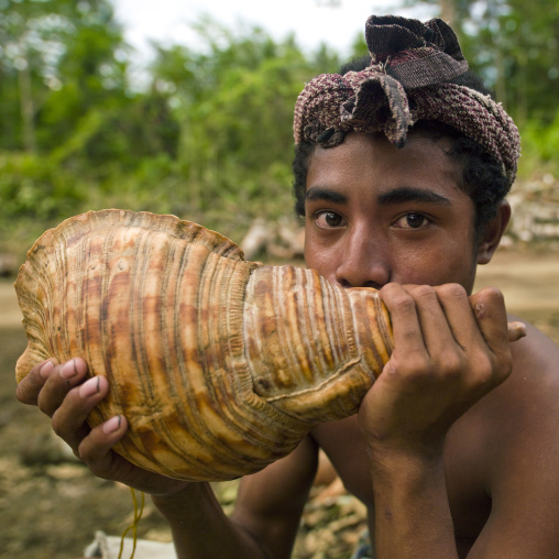 Boy blowing in a shell to call friends, Milne Bay Province, Alotau, Papua New Guinea