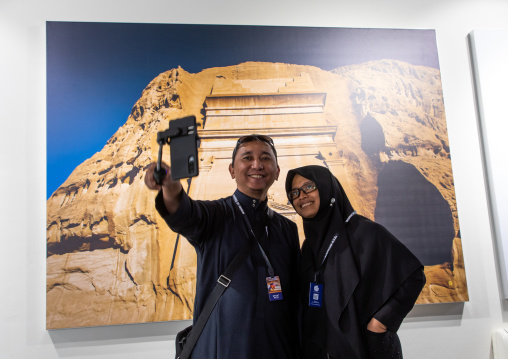Indonesian tourists taking a selfie in front of a picture of Madain Saleh, Al Madinah Province, Alula, Saudi Arabia