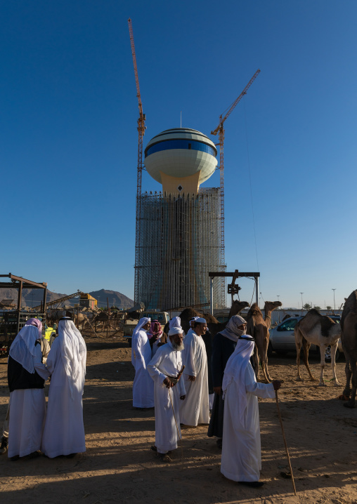 Saudi men in the camel market in front of a water tower, Najran Province, Najran, Saudi Arabia