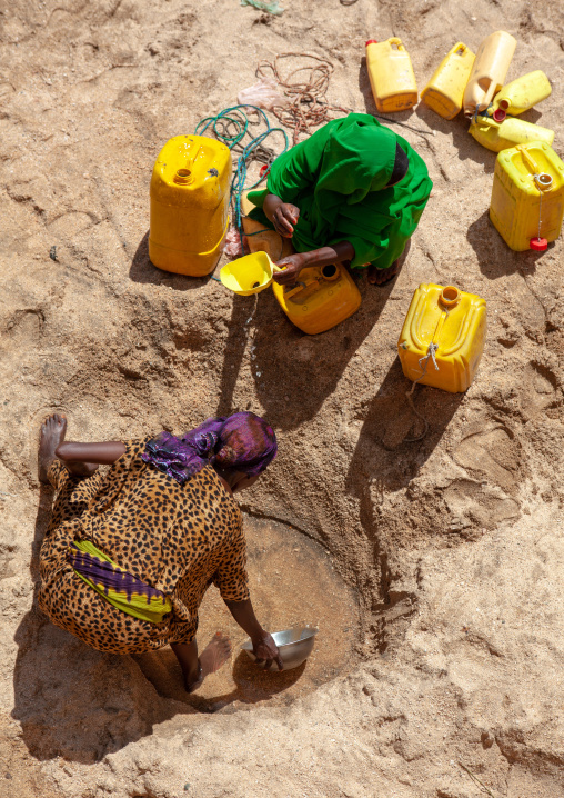 Somali women taking drinking water from a well hole in the sand and pouring it into plastic containers, North-Western province, Lasadacwo Village, Somaliland