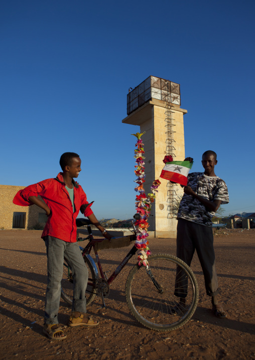 Two Teenage Boys Outside The Ruins Of The Burao Technology Institute Holding A Bike Covered With Plastic Flowers And A Somaliland Flag, Burao, Somaliland