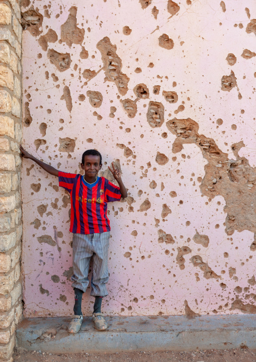 Somali boy with a barcelona football shirt in front of a wal full of bullets holes, Togdheer region, Burao, Somaliland