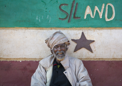 Portrait Of A Smiling Senior Man Wearing A White Beard And A White Turban In Front Of A Somaliland Flag Painted Onto A Wall, Baligubadle, Somaliland