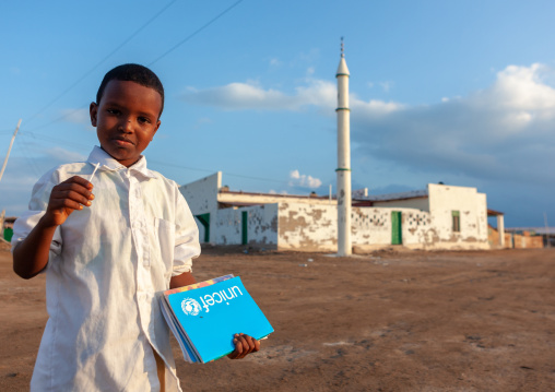 Somali boy with a unicef blue book in front of a mosque, Awdal region, Zeila, Somaliland