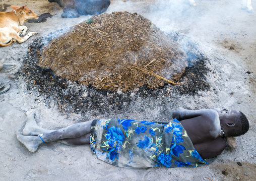 Mundari tribe man resting on a wooden pillow in front of a bonfire made with dried cow dungs to repel mosquitoes, Central Equatoria, Terekeka, South Sudan