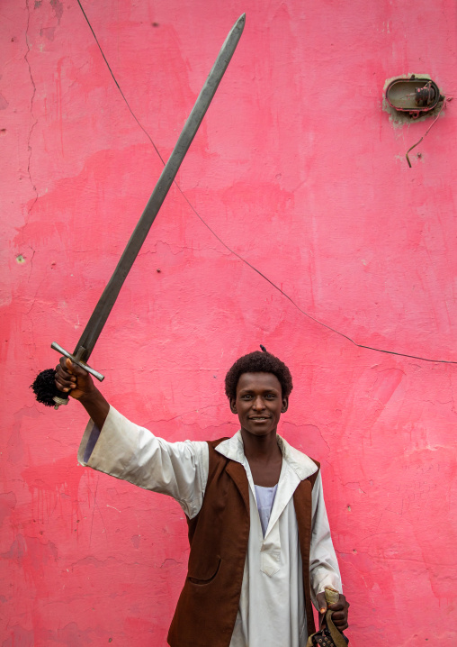 Beja tribe warrior with his sword in front of a pink wall, Red Sea State, Port Sudan, Sudan