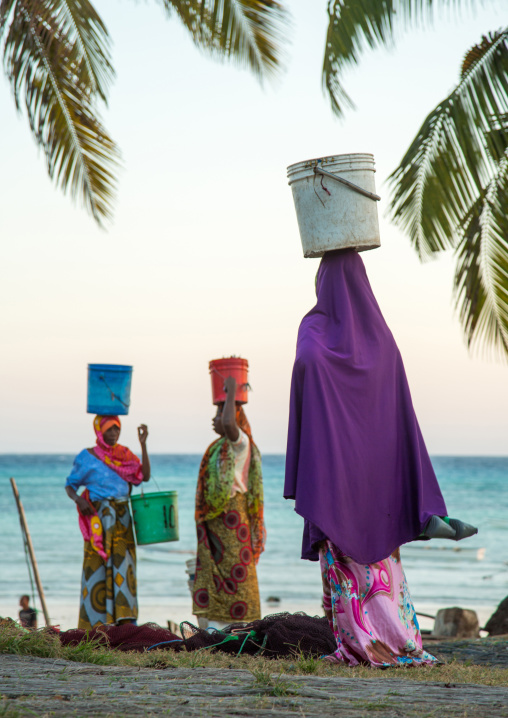 Tanzania, Zanzibar, Kizimkazi, women carrying fishes in a bucket on their heads