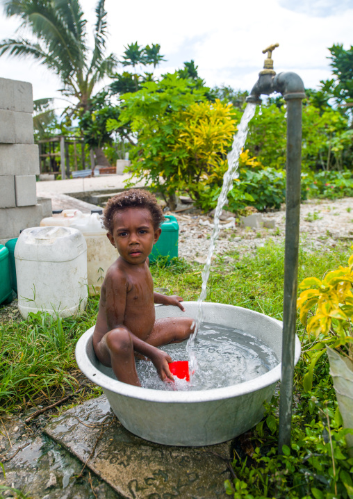 Child boy bathing in in a large metalic bowl in a garden, Efate island, Port Vila, Vanuatu